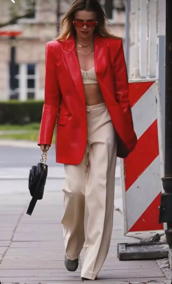 a bold look with a woven crop top, tan pants, a black bag with chain, an oversized red leather blazer