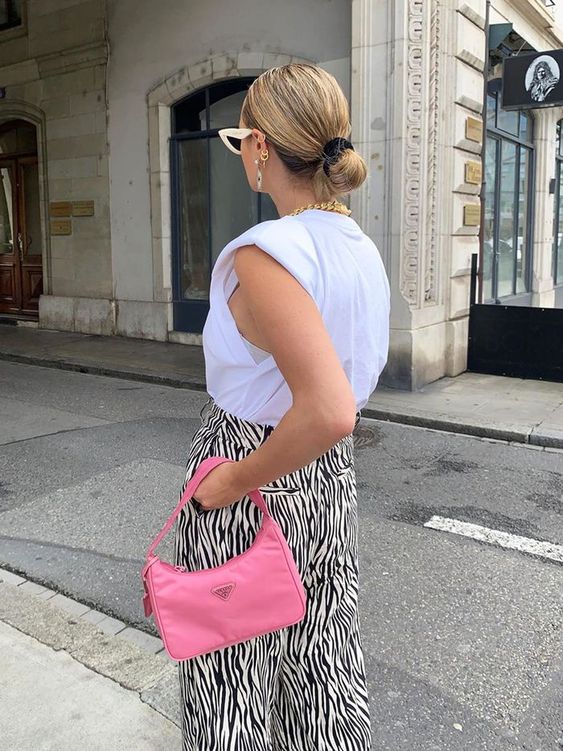 a bright summer look with a white top with accented shoulders, zebra print pants, a bold pink baguette bag