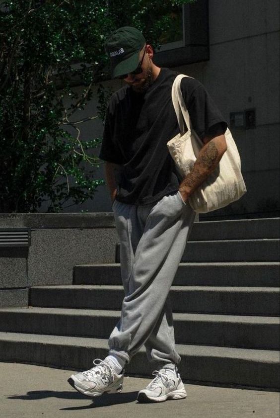 a sport look with a black t-shirt, grey sweatpants, white trainers and socks, a neutral canvas bag and a green cap