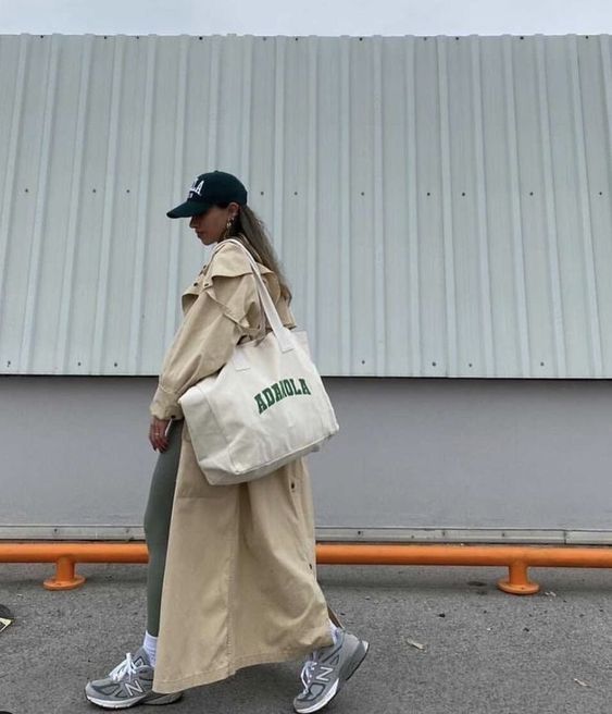 a sport chic outfit with green leggings, white socks, grey trainers, a beige maxi trench, a black cap and a neutral canvas bag