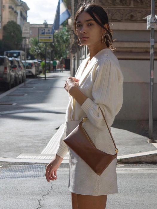 a neutral mini skirt, a neutral cardigan tucked into the skirt, a brown baguette bag plus statement earrings