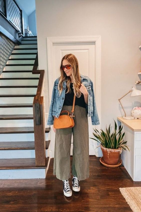a black top, khaki wideleg trousers, black high top sneakers, a blue denim jacket and an orange bag for spring