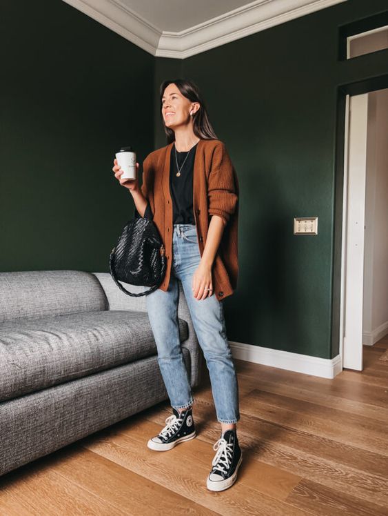 a black t shirt, blue cropped jeans, black high top sneakers, a rust colored oversized cardigan and a black woven backpack
