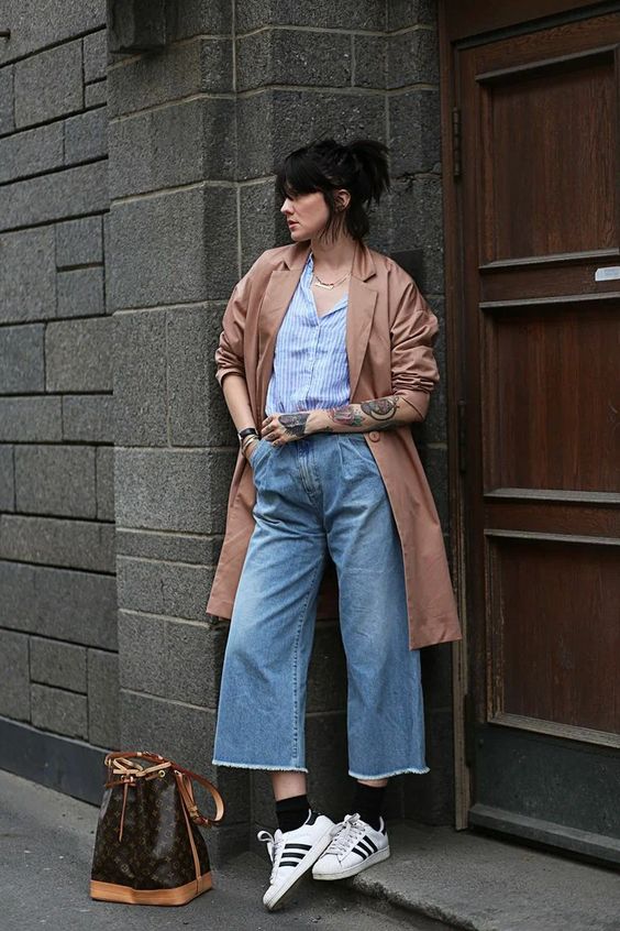 a blue striped shirt, blue wide leg jeans, white Gazelle sneakers, black socks, a copper trench and a printed bag