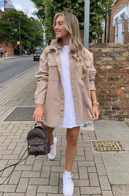 a white t-shirt dress, a tan denim jacket, white trainers and socks and a brown printed backpack for summer