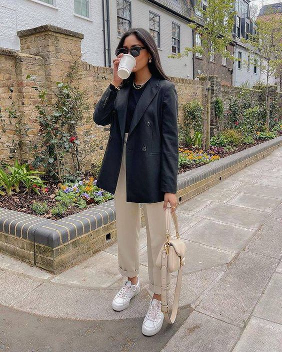 a black t-shirt, black blazer, tan trousers and a bag, white sneakers and a necklace are a cool work look