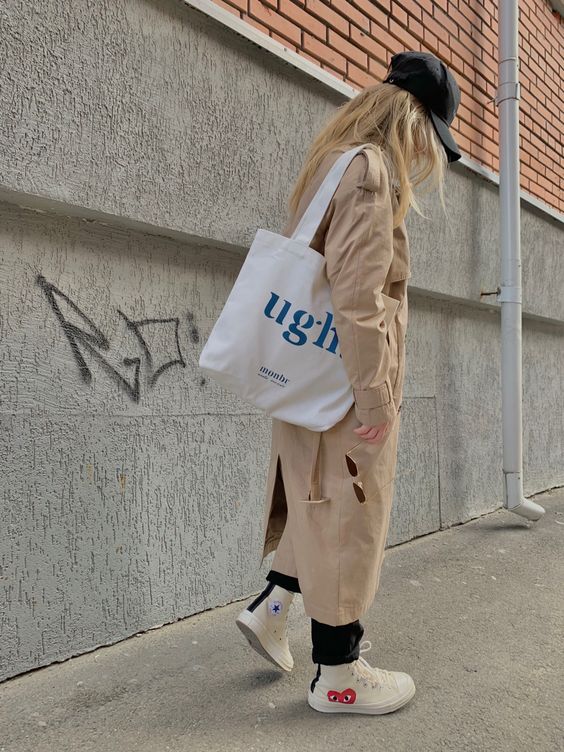 a beige trench, black jeans, a black cap, white sneakers, a white printed tote are a lovely look for spring