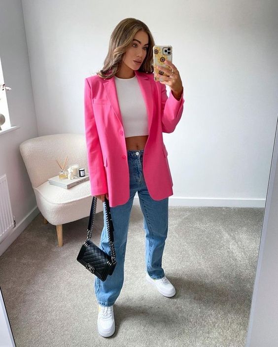 a simple and sexy outfit with a white crop top, blue jeans, white sneakers, a bright pink blazer and a black bag with chain