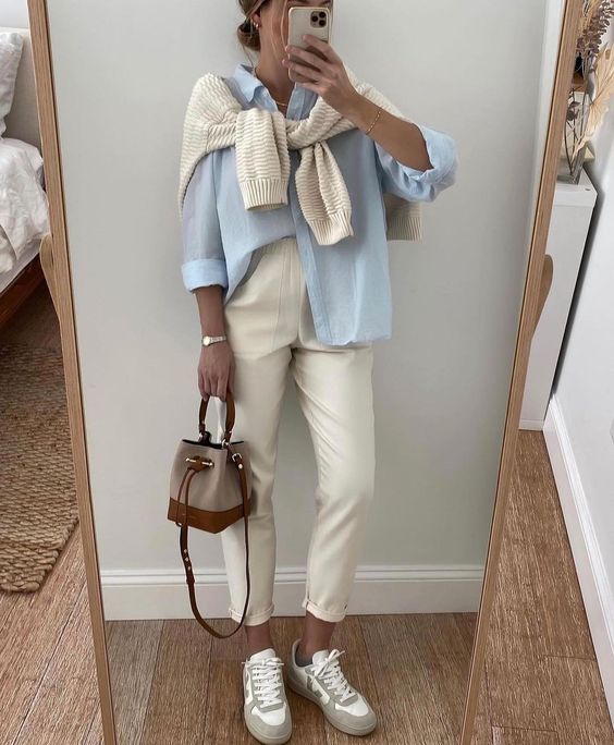 a blue shirt, neutral jeans, neutral trainers and a jumper over the shoulders, a two-tone bag for spring