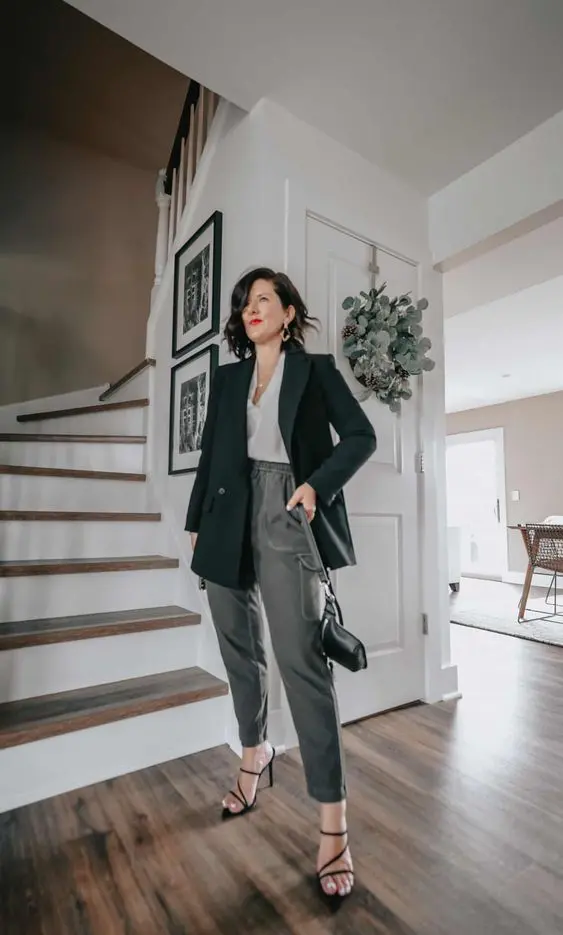 a chic outfit with grey pants, a black blazer, a white top, black strappy heels and a small black bag plus statement earrings