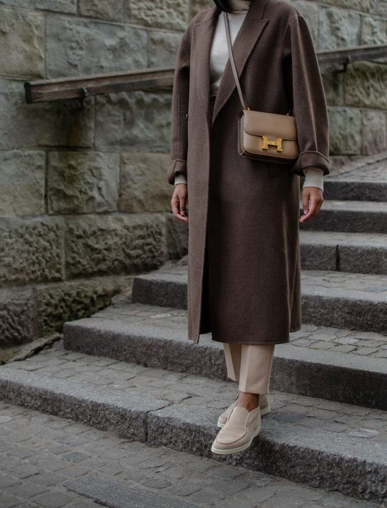 a neutral turtleneck, tan pants, tan loafers, a chocolate brown midi coat and a beige crossbody bag
