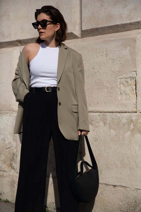 a stylish spring to summer work outfit with a white bodysuit, a greige oversized blazer, black pants, a black bag and a black belt