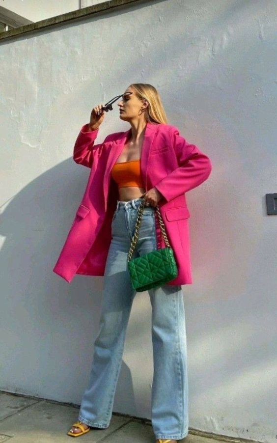 a colorful outfit with an orange crop top, bleached jeans, yellow shoes, an oversized pink blazer and a green bag with chain