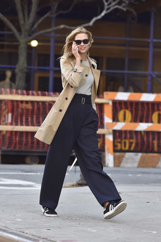 an elegant outfit with a neutral t-shirt, navy high waisted pants, black sneakers, a tan trench is a cool idea for spring