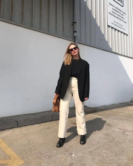 a work look with a black tee, tan jeans, black boots, an oversized black blazer and a brown bag