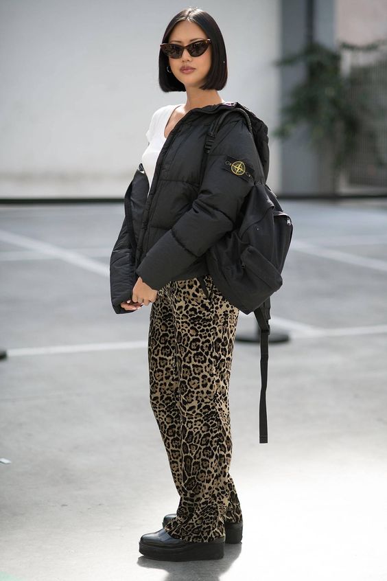 a creative sporty look with a white t-shirt, leopard print pants, black shoes, a black puffer and a black backpack