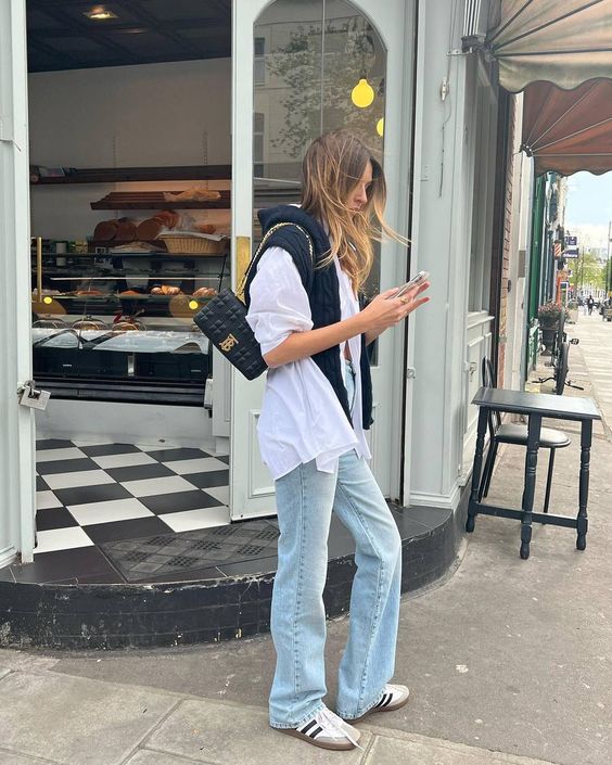 an oversized white button down, bleached jeans, a black jumper, neutral Adidas sneakers and a small black bag