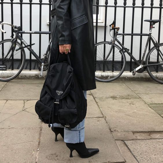 a 90s look with blue cuffed jeans, black heels, a black leather trench and a black backpack