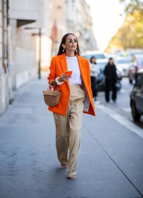 a bold spring work look with a white t-shirt, tan trousers, an oversized orange blazer, strappy shoes and a beige mini bag