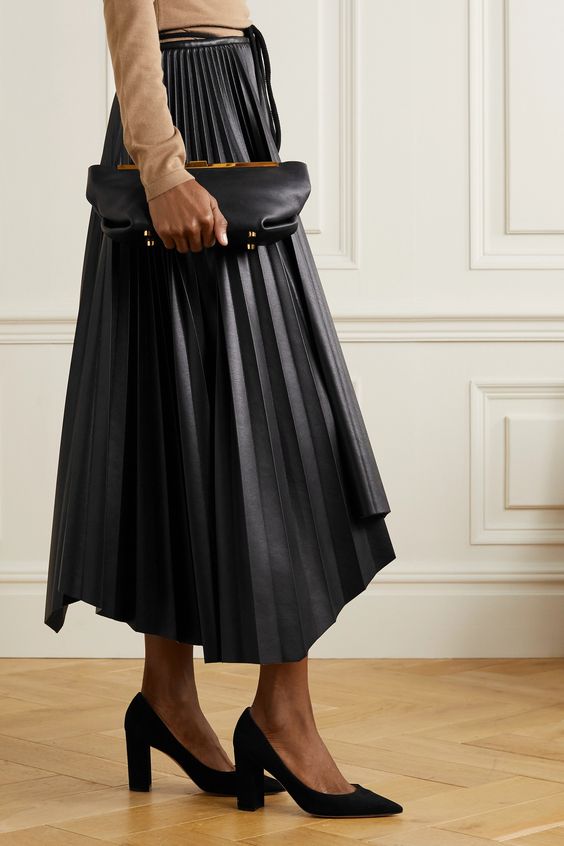 a tan long sleeve top, a black leather pleated midi skirt, black shoes and a modern black clutch