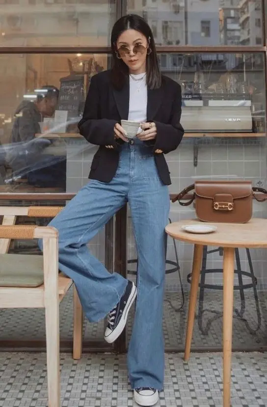 a white t-shirt, a black blazer, blue high waisted flare jeans, black sneakers and a chain necklace plus a chic brown bag