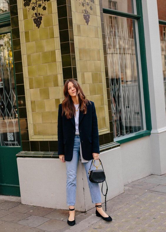 a white t-shirt, blue cropped jeans, black ankle strap shoes, an oversized blazer and a small black bag with a ring handle