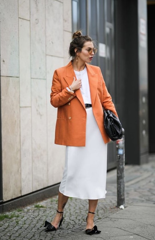 whimsy black shoes, a white tee, a white midi skirt, an orange oversized blazer and a large black clutch