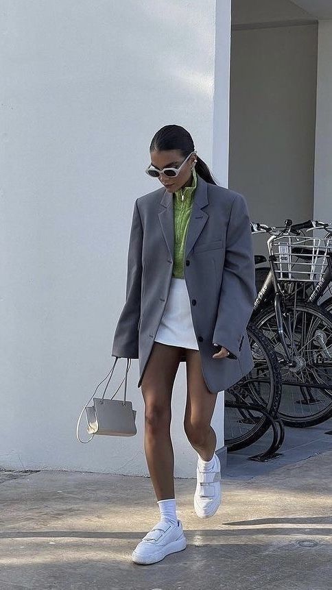 a neon green zip sweater, a white mini skirt, a grey oversized blazer, white trainers and socks, a white bag