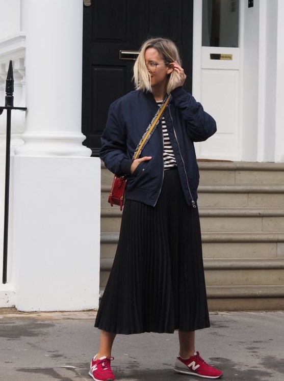 a navy and white t-shirt, a black pleated midi skirt, a navy bomber jacket, red trainers and a red crossbody bag