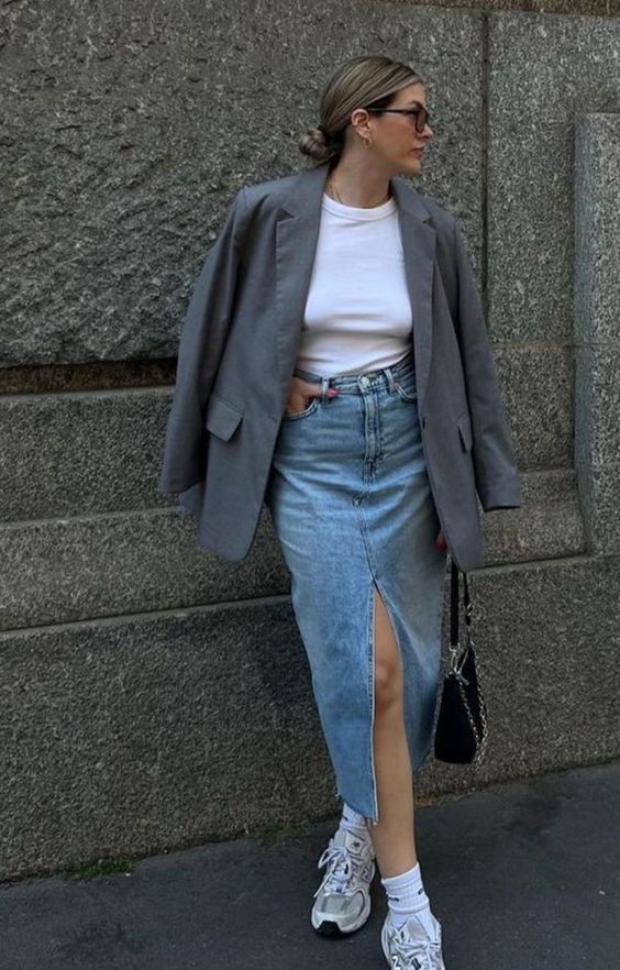 a white t-shirt, a blue denim midi with a front slit, grey trainers and white socks, a grey oversized blazer and a black bag