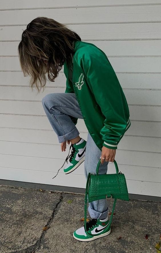 a green satin bomber jacket, bleached blue jeans, green Jordan sneakers, a green reptile leather mini bag