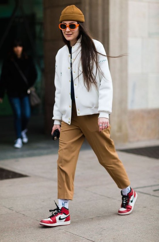 a white bomber jacket, rust-colored cropped trousers, red trainers, white socks and a mustard beanie on top