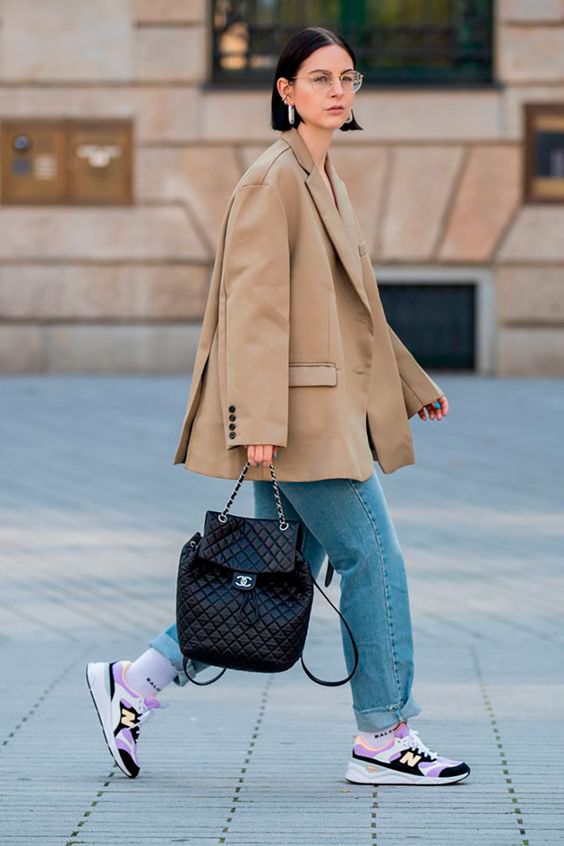a chic spring look with an oversized beige blazer, blue jeans, purple New Balance sneakers and a black bag