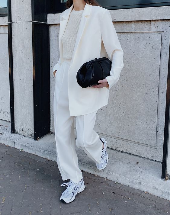 a creamy pantsuit, a neutral top, grey New Balance trainers and a black clutch