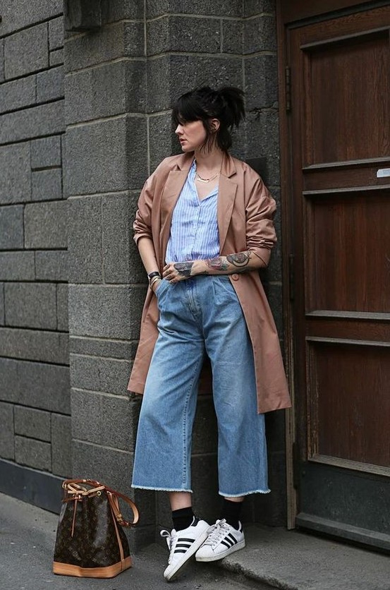 a blue striped shirt, blue wide leg jeans, white Gazelle sneakers, black socks, a copper trench and a printed bag