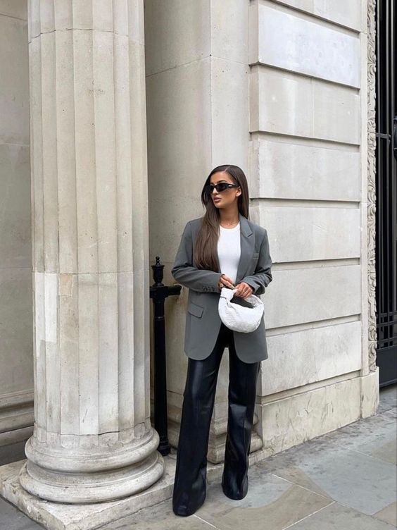 a minimalist outfit with a white bodysuit, black leather pants, an oversized grey blazer and a white woven bag is suitable for work