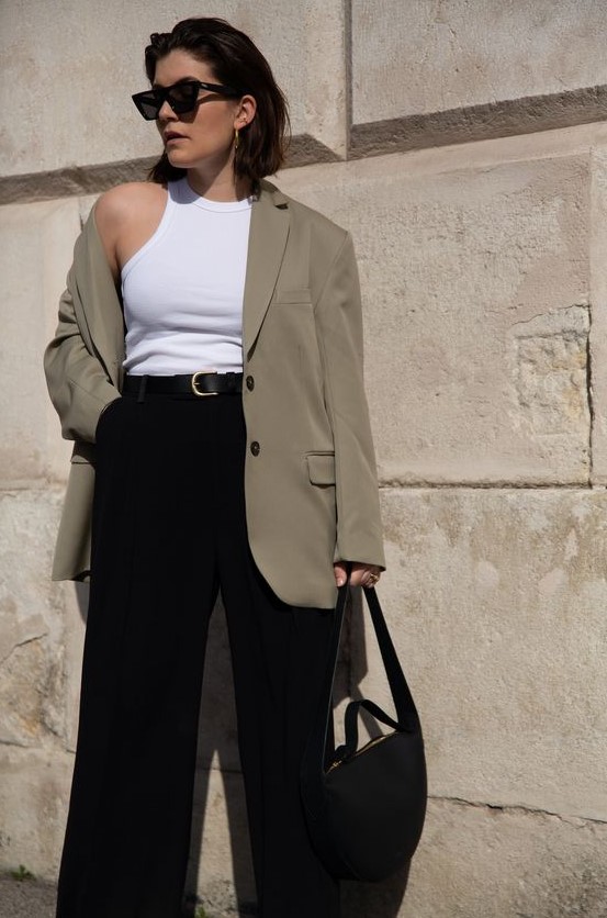 a stylish spring to summer work outfit with a white bodysuit, a greige oversized blazer, black pants, a black bag and a black belt