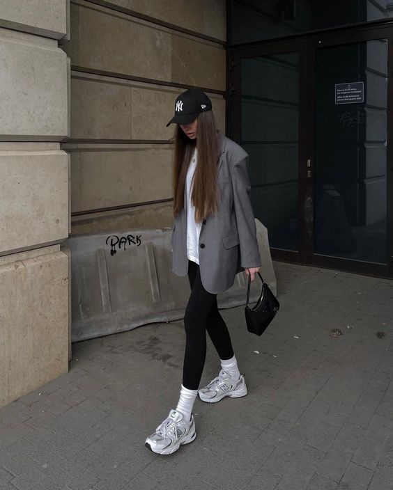 a white oversized tee, black leggings, grey trainers and white socks, an oversized grey blazer, a black cap and a black bag