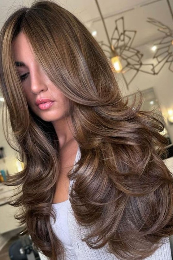 a beautiful long brunette butterfly haircut with curtain bangs and a bit of golden blonde balayage is amazing