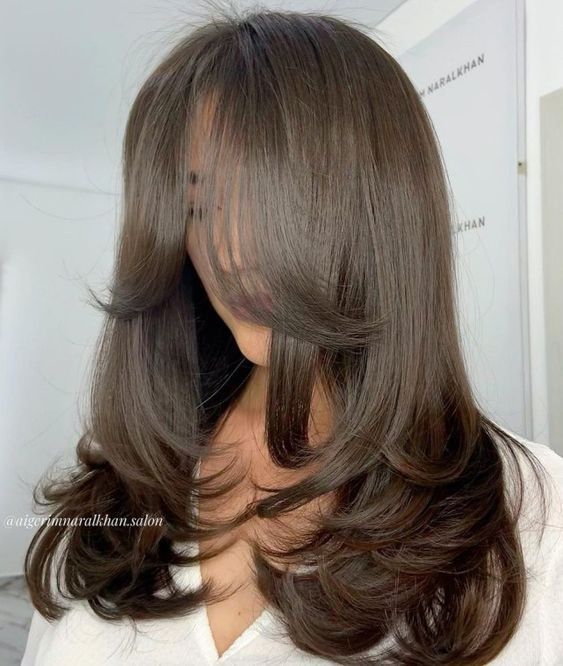 a classy butterfly haircut on dark brown hair, with layers and curved ends, with curtain bangs is pure chic and elegance