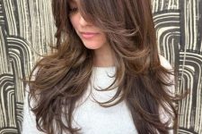 a long brunette butterfly haircut with caramel balayage and bottleneck bangs and curled ends is amazing