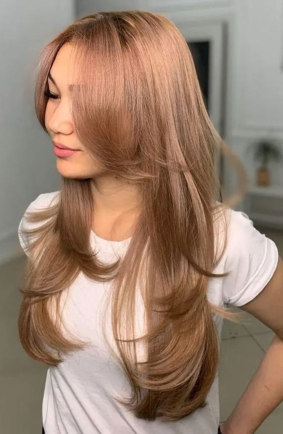 a long butterfly haircut with a delicate peachy pink shade, long curtain bangs and curled ends is wow