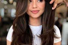 a long dark brunette butterfly haircut with caramel balayage and long curtain bangs plus curled ends is veyr girlish