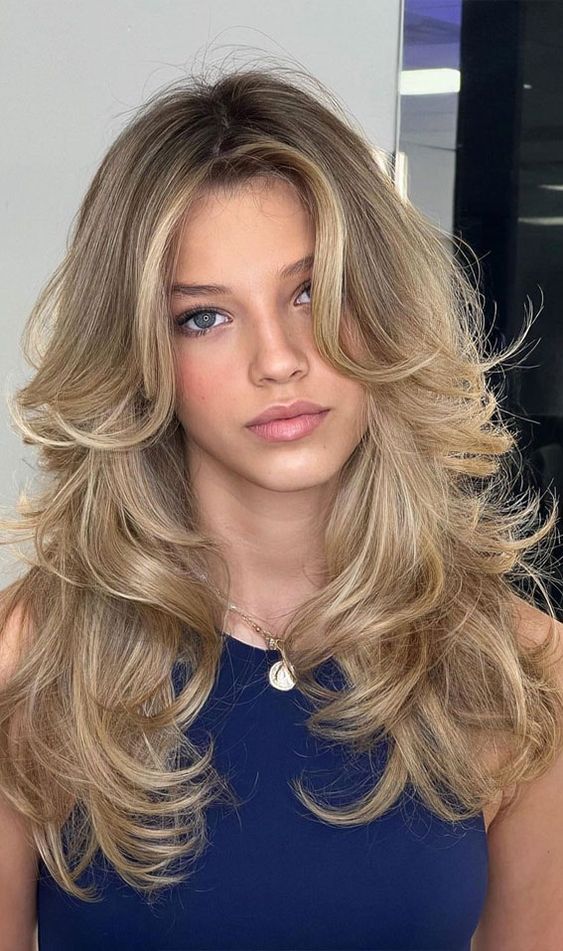 a long golden blonde butterfly haircut with curled ends and slight contouring plus a lot of volume