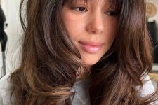 a lovely dark brunette butterfly haircut with wispy bangs, caramel balayage and dimension and waves is amazing