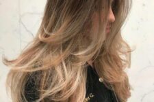 brown hair with a darker root and blonde highlights and ombre, with a butterfly haircut for a feathered and chic look