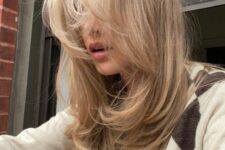 chic blonde long hair with highlights and bangs, with a butterfly haircut and feathered layers and curved ends