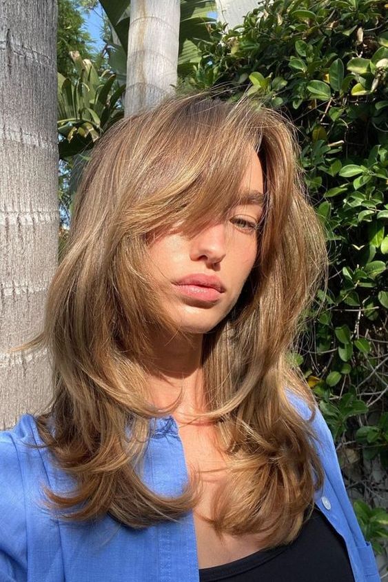 long bronde hair with a butterfly haircut, with caramel highlights and face-framing locks and curved ends