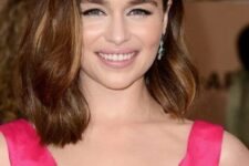 Emilia Clarke wearing a brown outgrown bob with caramel and honey highlights, side part and soft waves is a very elegant idea