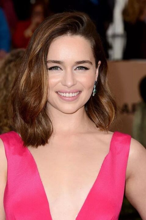 Emilia Clarke wearing a brown outgrown bob with caramel and honey highlights, side part and soft waves is a very elegant idea